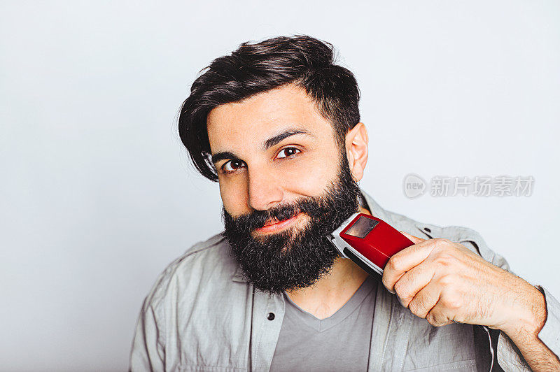 年轻的大胡子男子与电动剃须刀摆姿势