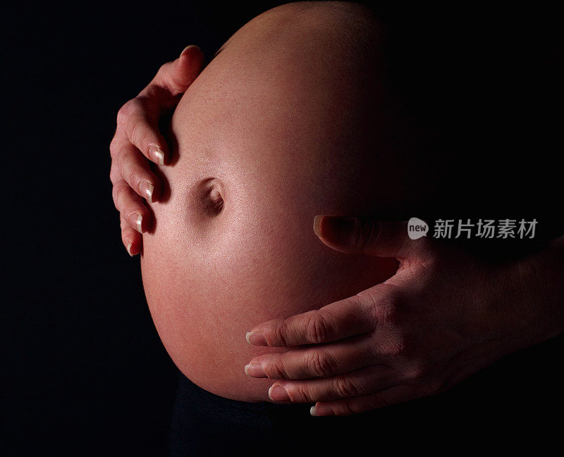 在黑色背景下，孕妇抱着裸露的腹部