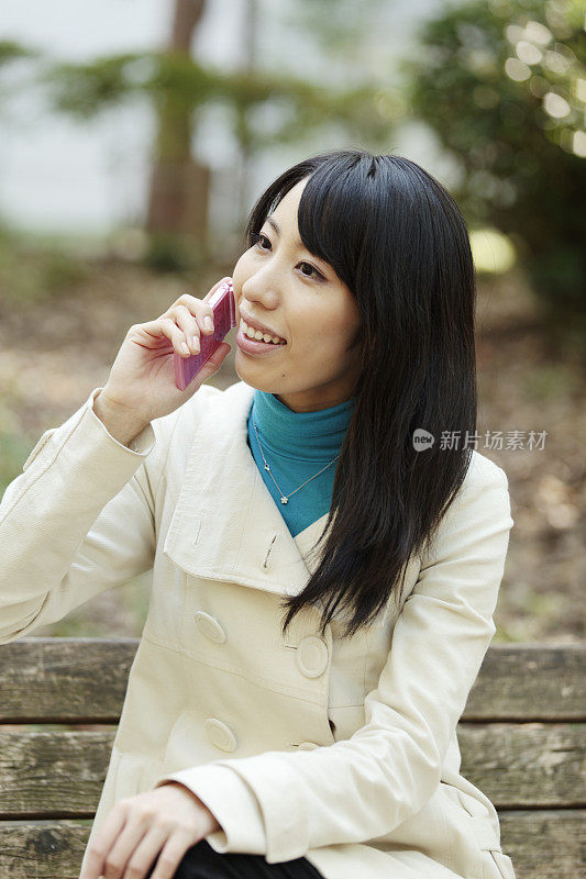 年轻的日本女性成年人在公园的长凳上讲手机