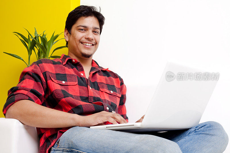 一个年轻的印度男性愉快的使用笔记本沙发沙发
