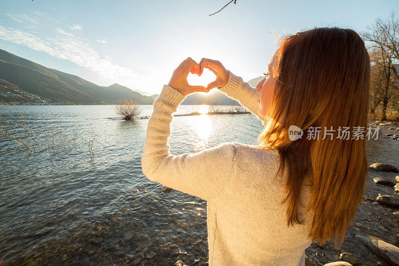 年轻女子在湖边做心形手指架