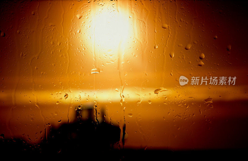 雨滴落在窗户上，夕阳和汽车在背景中