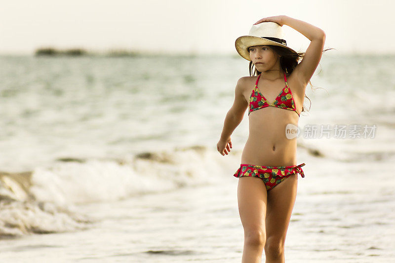 穿着比基尼的小女孩在沙滩上戴着草帽