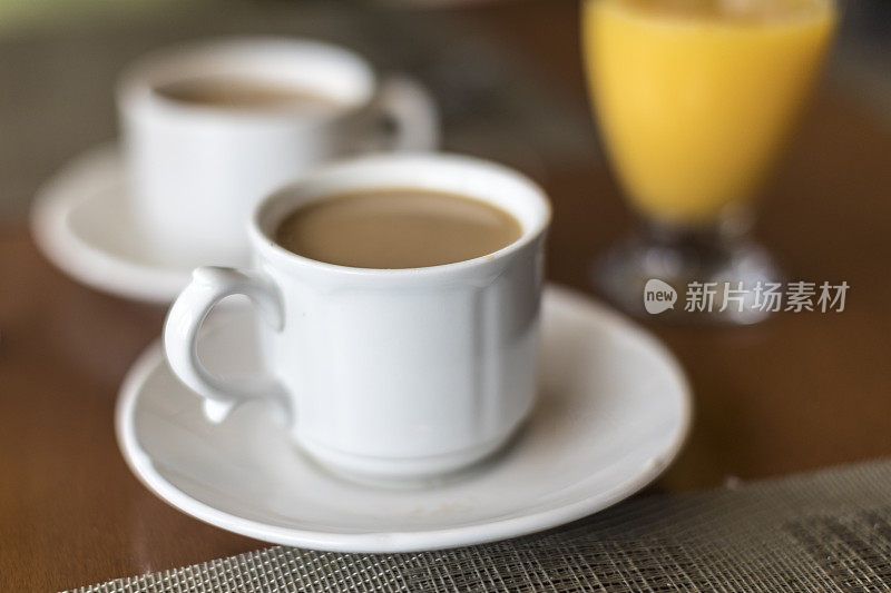特写的两杯咖啡与牛奶或奶油在白瓷杯和一杯橙汁的背景。