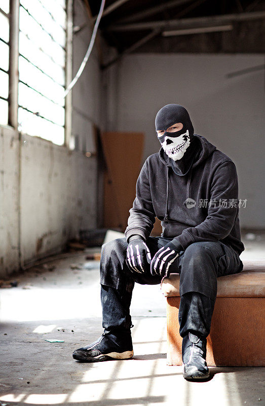 蒙面人坐在一个废弃的仓库里