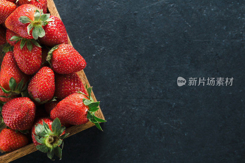 俯视图的一个木制的盒子与成熟的新鲜草莓在一个黑色的桌子上。放置文本。健康食品的概念。