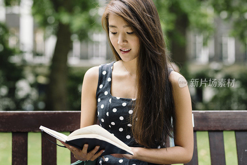 在伦敦公园的年轻亚洲人阅读笔记