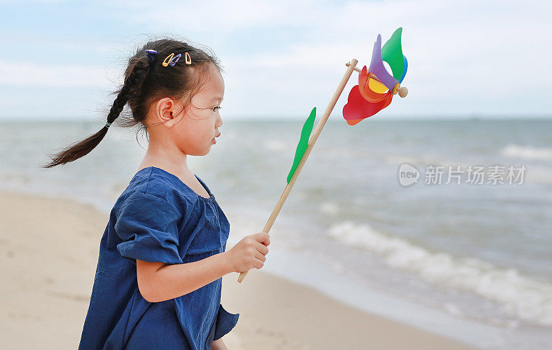 亚洲小女孩在沙滩上玩五颜六色的风车玩具。