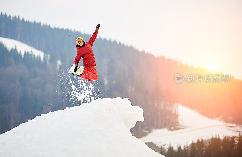 一名男性滑雪板运动员在雪山的顶端跳着滑雪板，对着镜头微笑。滑雪和单板滑雪的概念