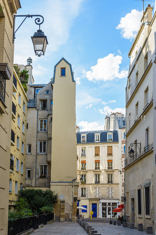 在巴黎历史中心的一条小步行街上的一个狭窄的建筑，在蓝色的天空下有古老的街灯