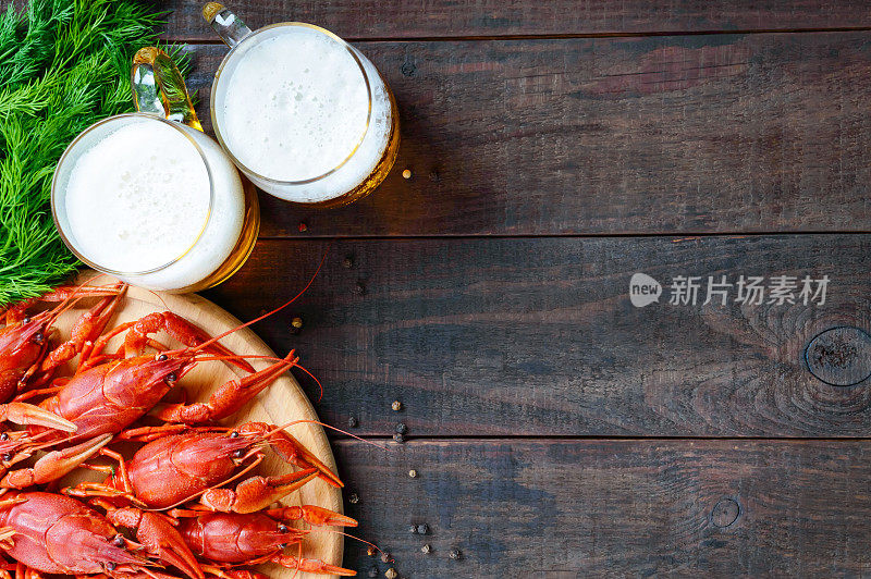 一堆美味的煮小龙虾放在一个圆形的木托盘上，两杯冰啤酒放在深色的背景上。前视图。为题字预留空间。