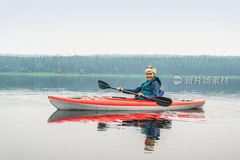 女人高兴地从红色的皮划艇上划到平静的湖面上