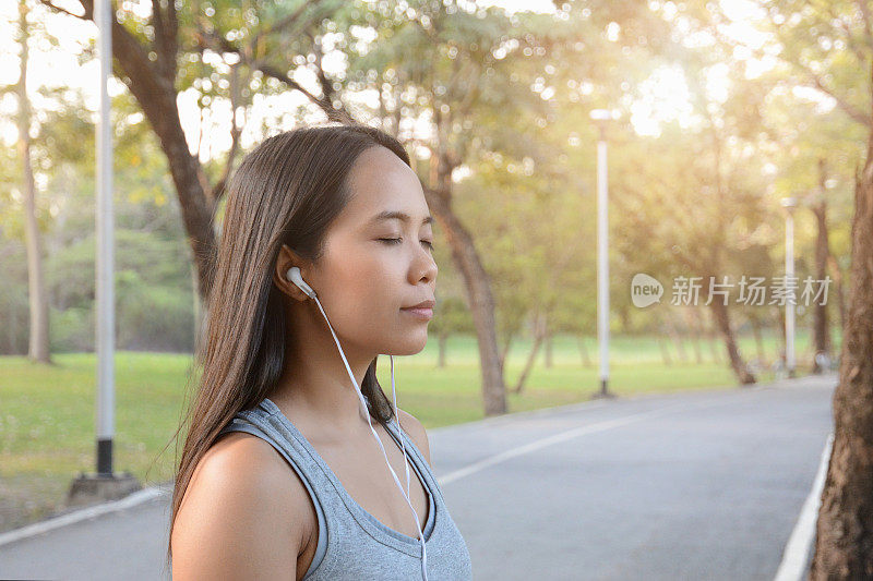 美丽的亚洲女人在公园里跑步，戴着耳机，闭着眼睛。