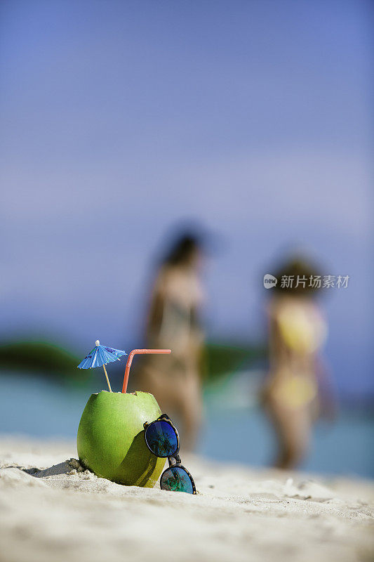 在加勒比海岛屿的绿松石沙滩上，戴着墨镜喝着椰子热带饮料