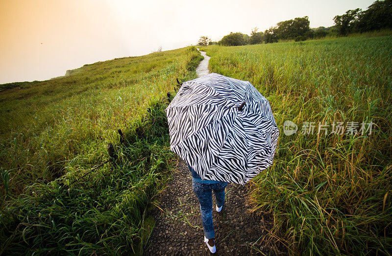 女性与伞顶视图之间的小路在日落的草地