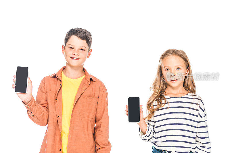 正面的两个微笑的孩子拿着智能手机与空白屏幕隔离在白色