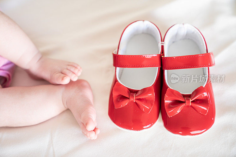 婴儿脚和红色的第一双鞋在床上的近距离照片
