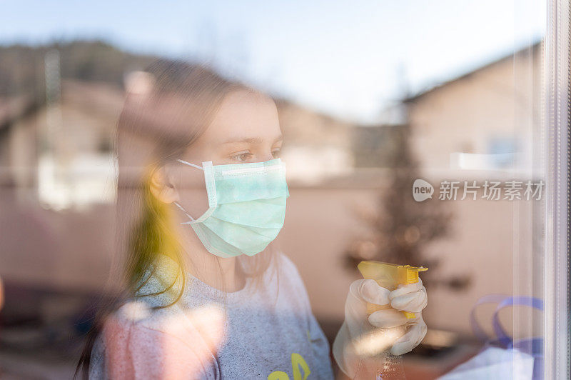 年轻的女孩戴着外科口罩和防护手套在家里擦窗户