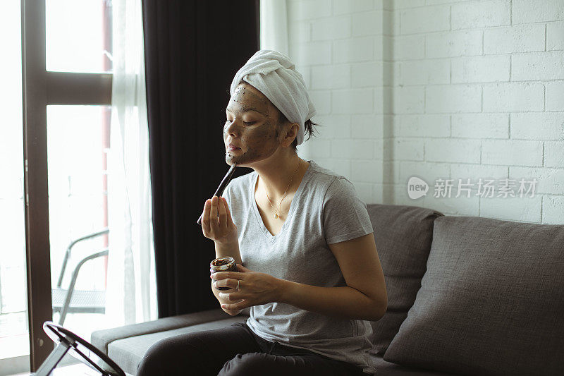 迷人的年轻女子用浴巾和面膜包裹在脸上