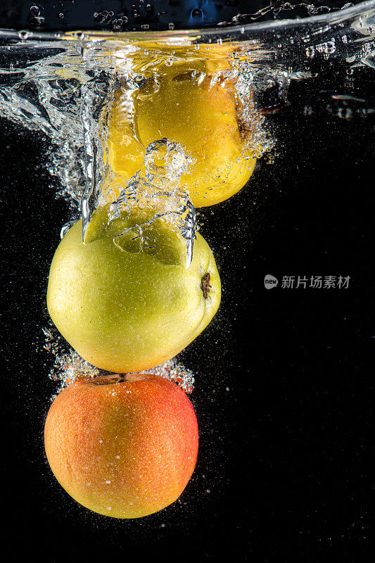 几个不同的苹果在水中溅起水花，冒着泡泡掉进鱼缸里