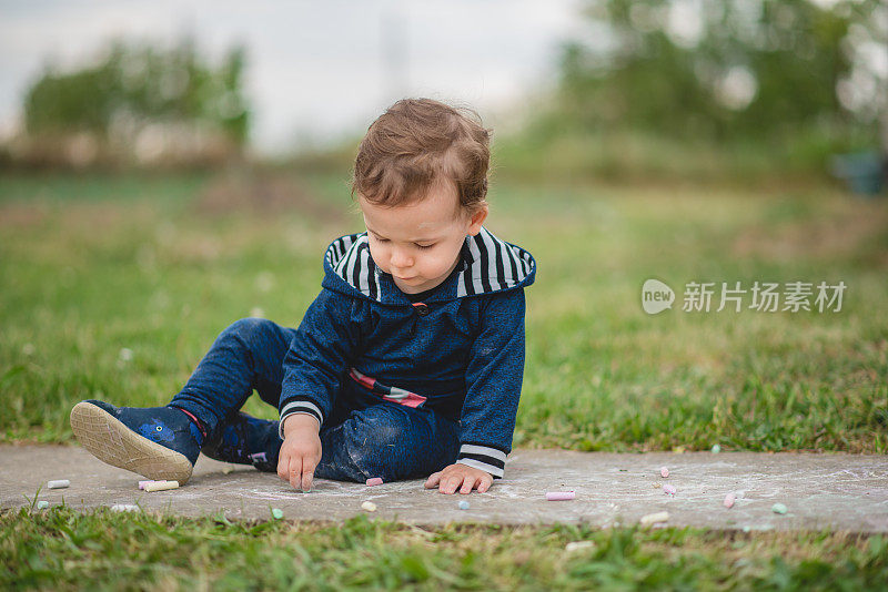 小男孩在户外玩耍，坐在草地上用粉笔画画