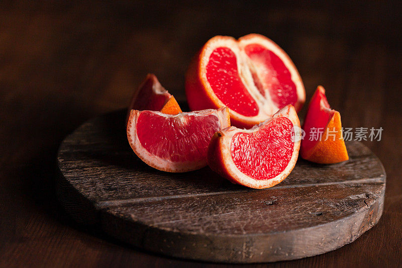 新鲜熟透的有机葡萄柚片放在质朴的木板上。天然维生素来源，低热量美味甜品。暗背景，近景，正面视图，微距