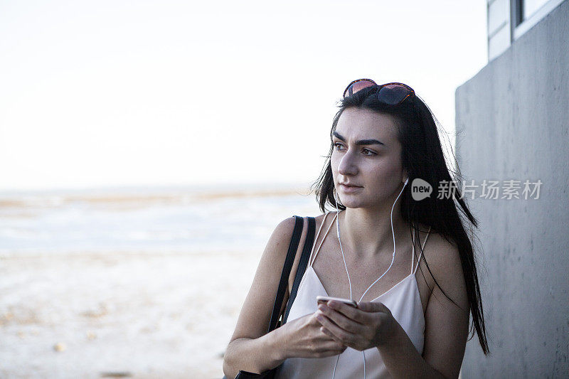 一个少女在夏天靠在墙上用智能手机，背景是大海