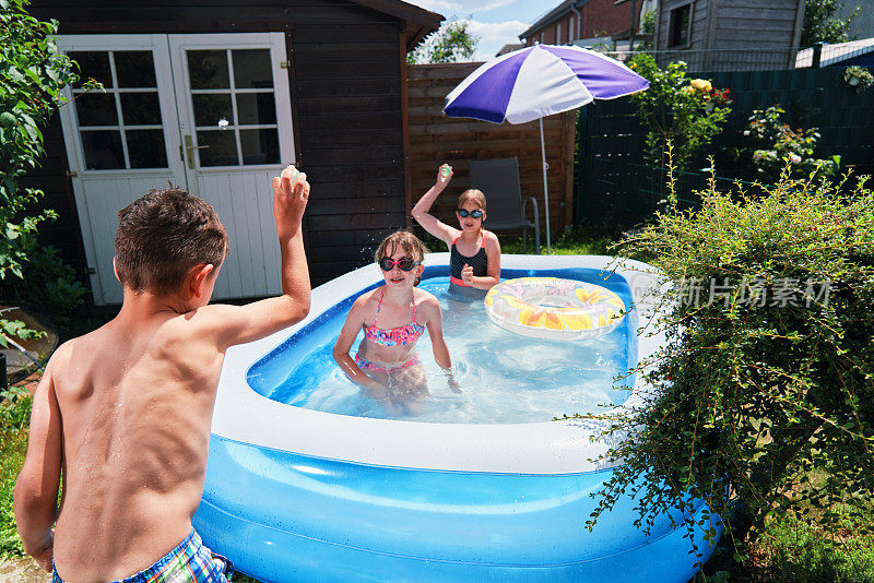 后院水的乐趣可爱的小孩玩水气球在游泳池