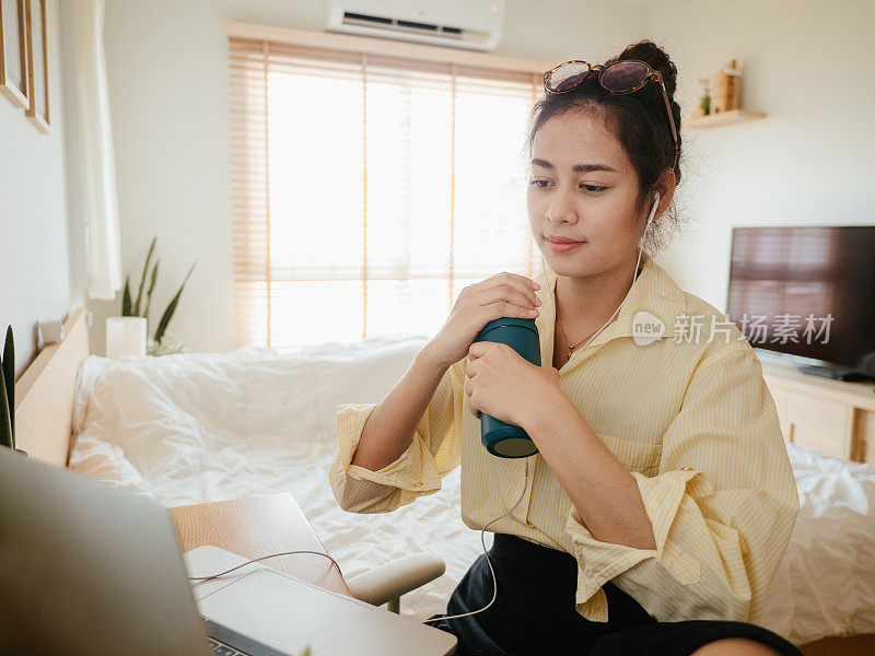 一位亚洲女性在家里开电话会议时使用笔记本电脑。