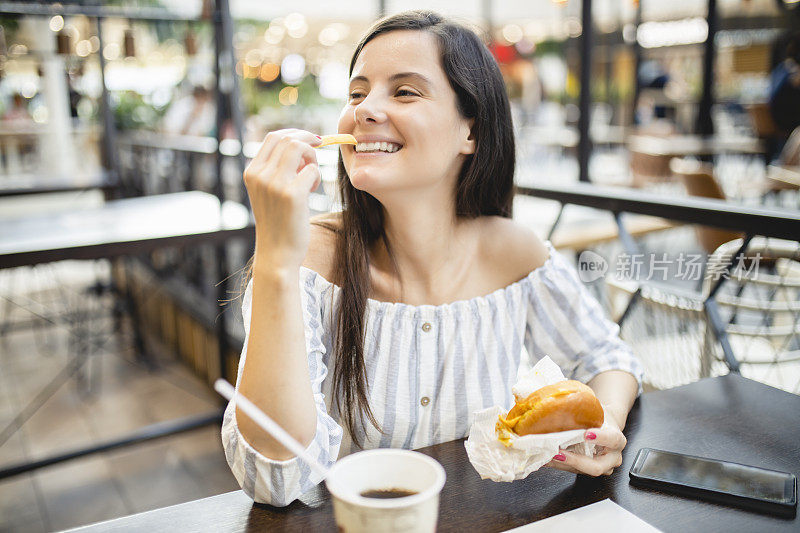 快乐的女人在快餐店吃午餐，吃汉堡包和喝苏打水