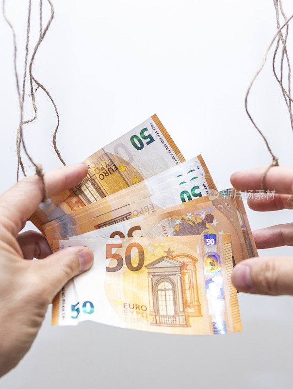男子手中握着欧元钞票。绳子绑在一个人的手上，像个木偶。