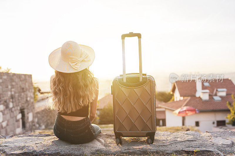 年轻的金发女人提着箱子在街上旅行