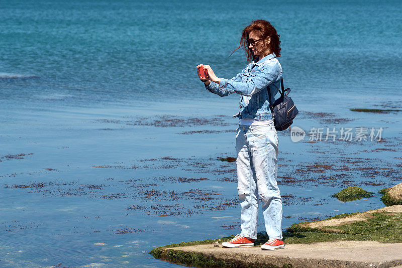 女游客在海边用智能手机拍照