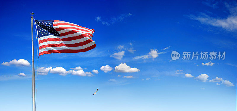 在晴朗的蓝天下，高高的旗杆上悬挂着美国国旗