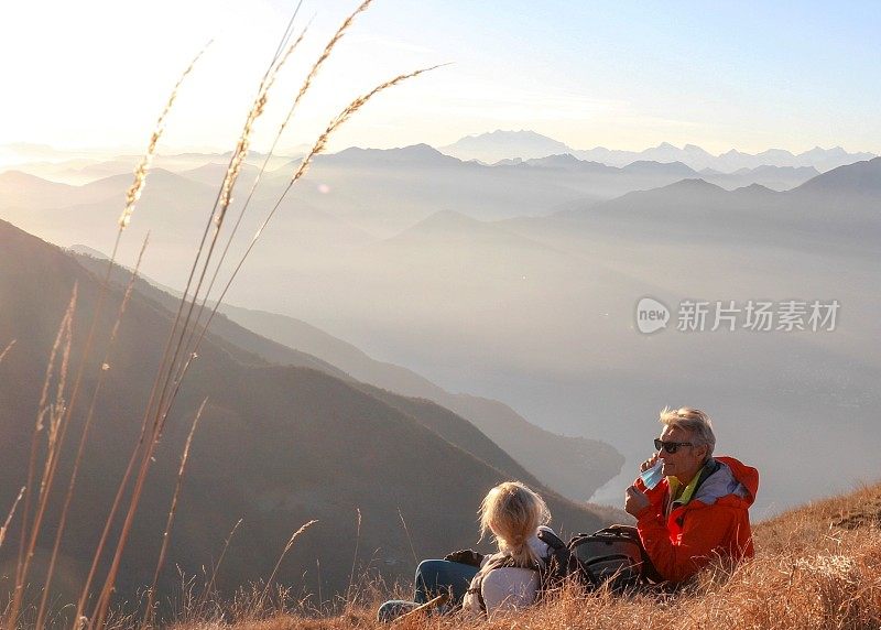 早晨，成熟的情侣徒步旅行者在长满草的山坡上放松