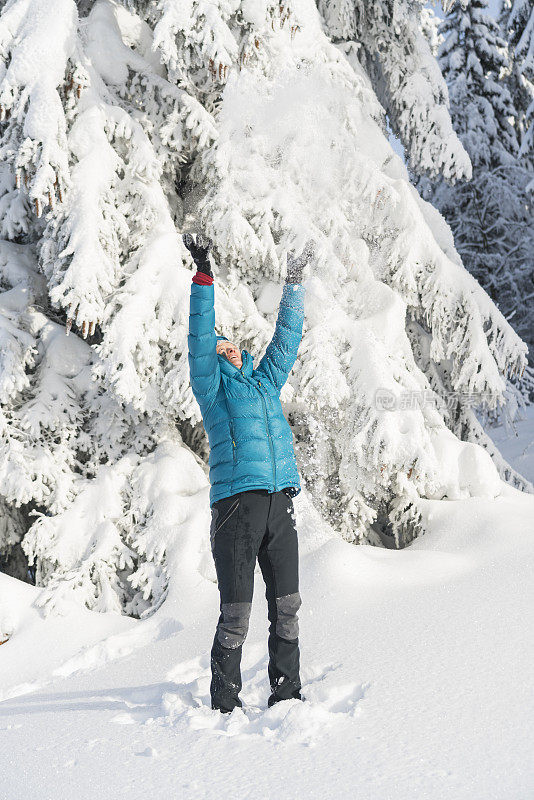 在冬天的森林里，成熟的女人穿着皮大衣向空中抛雪