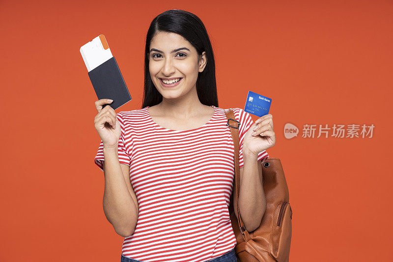 年轻女学生的肖像持有信用卡和显示护照票站在孤立的红色背景:股票照片