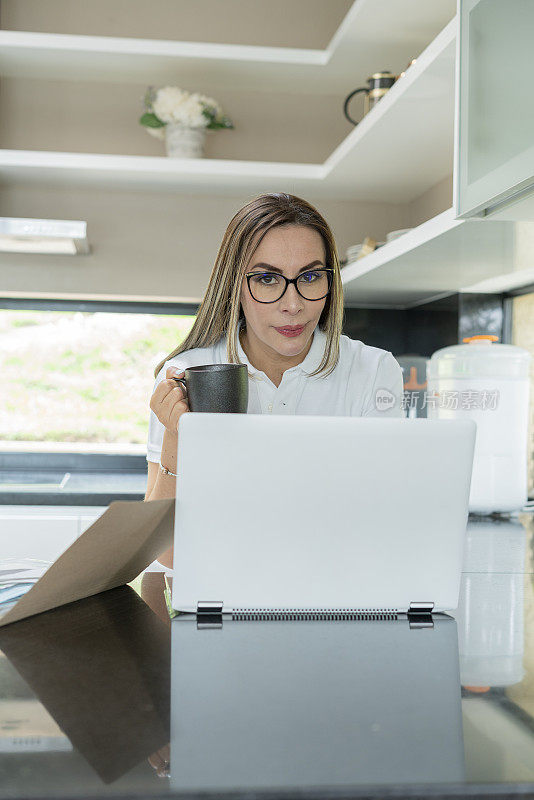 一个女人穿着舒适的衣服，在厨房用笔记本电脑检查她的财务状况