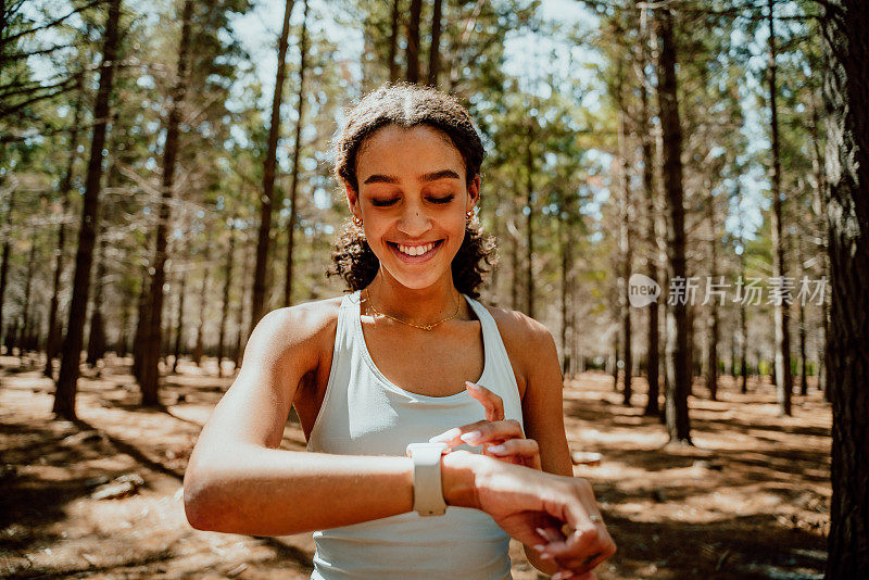微笑混合种族女性在森林中检查智能手表