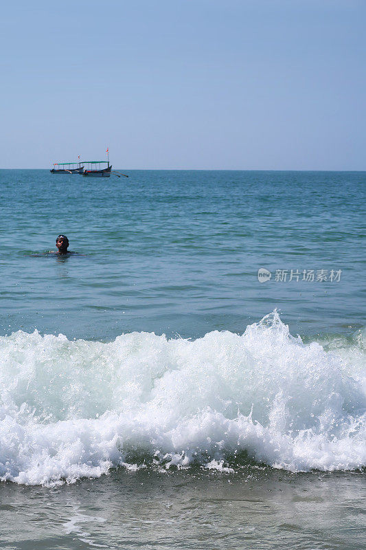 在印度果阿的Palolem海滩，一名印度男子在海滩度假，当海浪翻滚到沙滩上时，他坐在印度洋上戏水