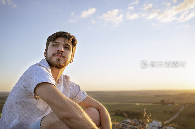 夕阳西下时，一个年轻人站在山顶眺望地平线。想象未来。