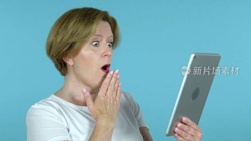 老妇人在蓝色背景上使用平板电脑时受到了惊吓