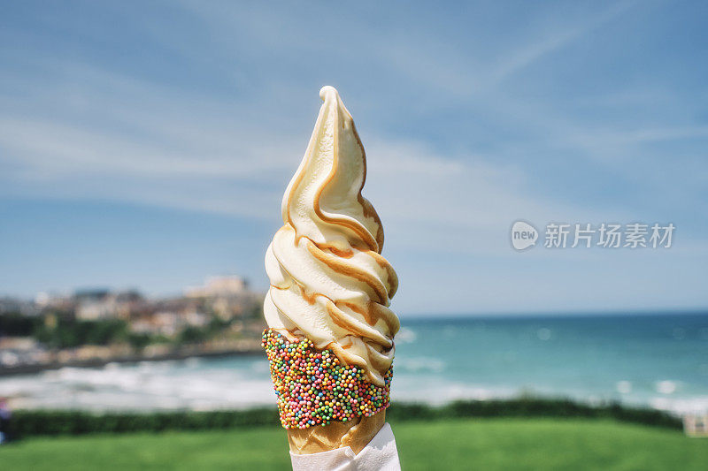 一个阳光明媚的夏日，康沃尔郡纽基镇的托湾海滩上，涂着焦糖酱的蛋筒冰淇淋。