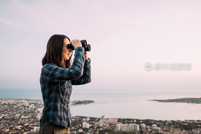 一个女人用双筒望远镜望着海湾。