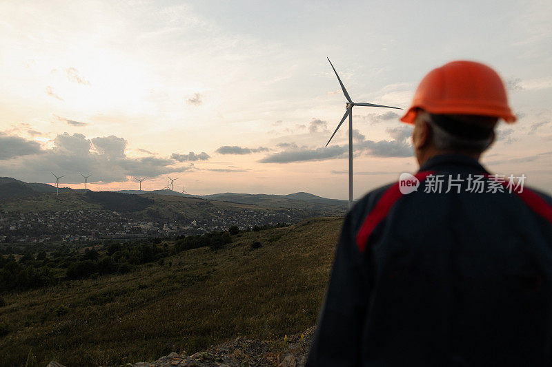 日落时分，高级工程师在山上观察风力涡轮机