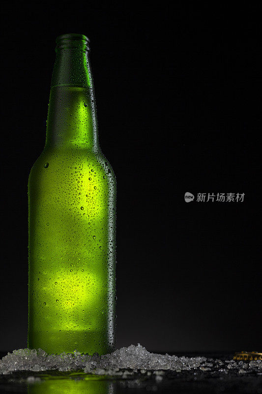 冰凉的绿色啤酒瓶，上面覆盖着冰和水滴-凝结。用于饮料饮料产品设计模型的毛坯。站在黑色背景的黑色桌子上。