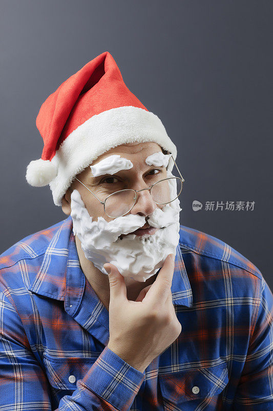 一个盛装打扮的圣诞老人，留着白色泡沫胡须，眯着眼睛，用手指托着下巴。假的圣诞老人。圣诞节的海报