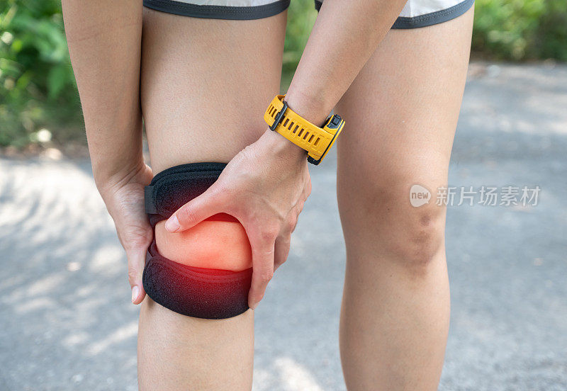 女运动员在膝盖疼痛时抱着膝盖当膝盖疼痛时她戴着支撑膝盖的支架。