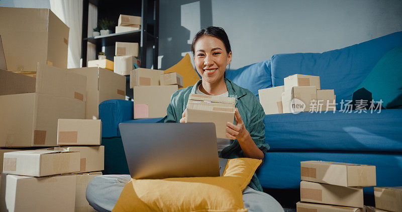年轻的亚洲女售货员在网上商店使用笔记本电脑准备包裹，以装运到客户在家里。