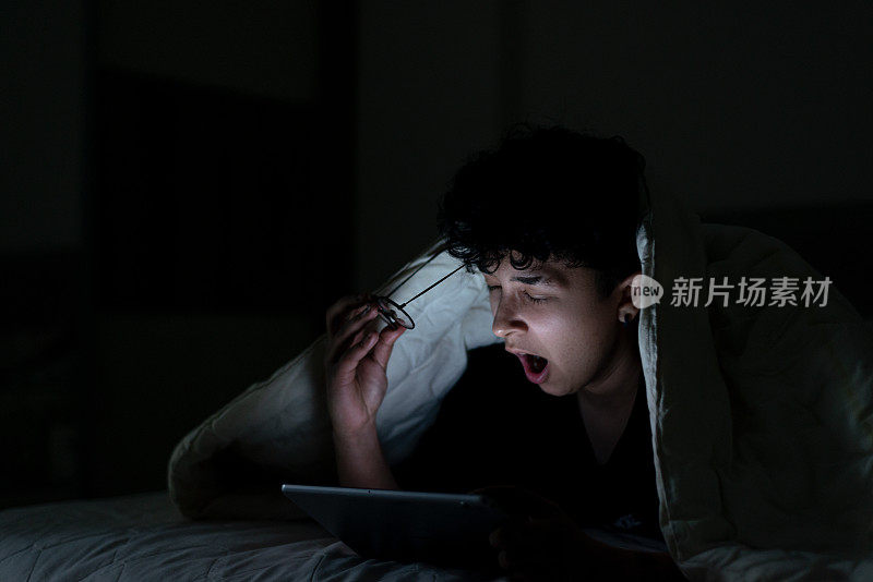 一个十几岁的女孩深夜在床上用智能手机，脸上带着睡意
